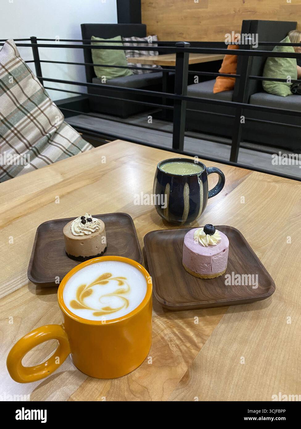 Kaffee und Desserts auf Holztisch in gemütlicher Café-Umgebung mit Sitzgelegenheiten im Hintergrund. Mobiles Foto Stockfoto