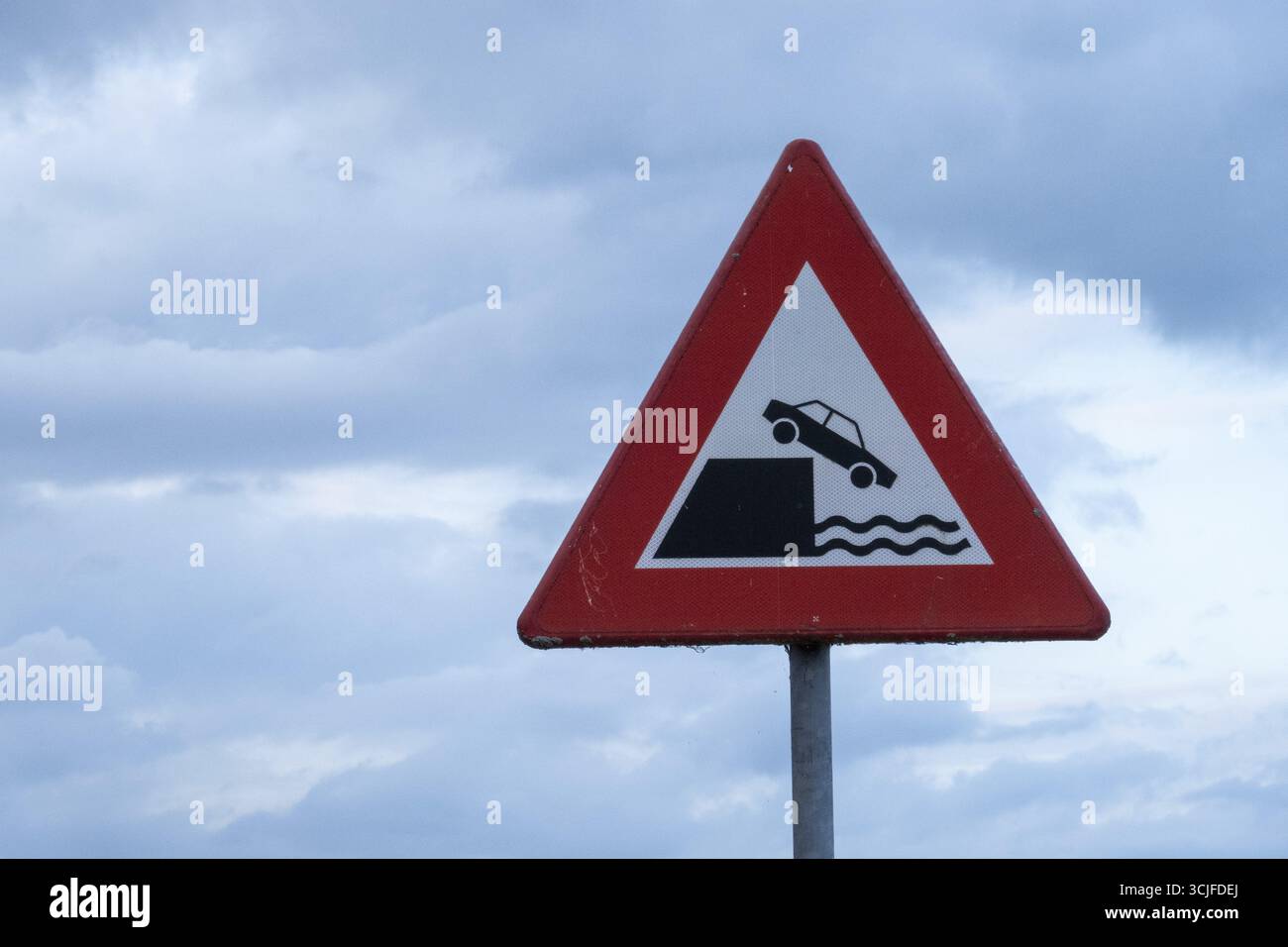 Rotes dreieckiges Warnschild, das die Gefahr anzeigt, dass das Fahrzeug in Wasser fällt, und vor bewölktem Himmel steht Stockfoto
