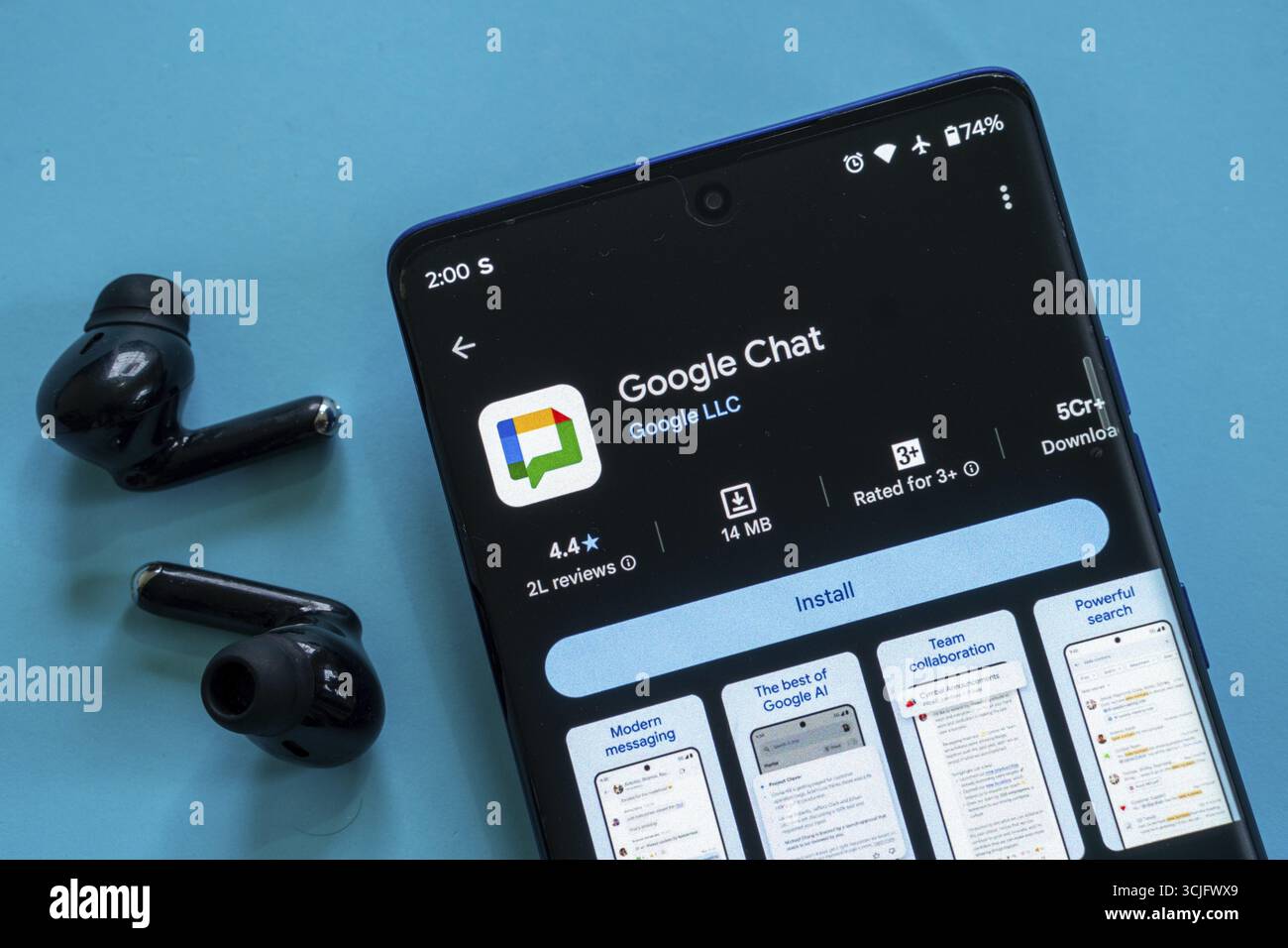 Smartphone zeigt die Google Chat App mit schwarzen Ohrstöpseln in der Nähe auf einer blauen Oberfläche an Stockfoto