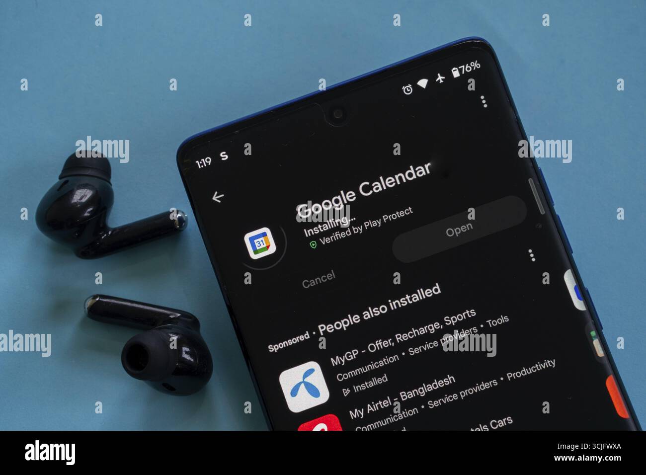 Smartphone zeigt den Installationsprozess des Google Calendar neben den Ohrhörern an Stockfoto