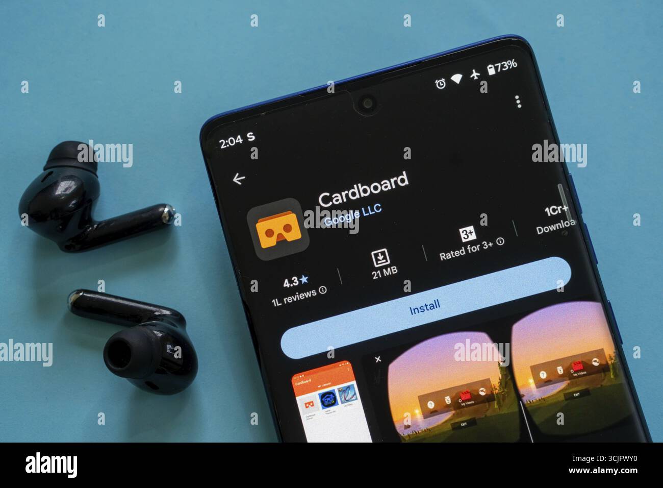 Die App aus Karton von Google wird auf dem Smartphone mit der Option zur Installation angezeigt, Ohrhörer sind im Lieferumfang enthalten Stockfoto