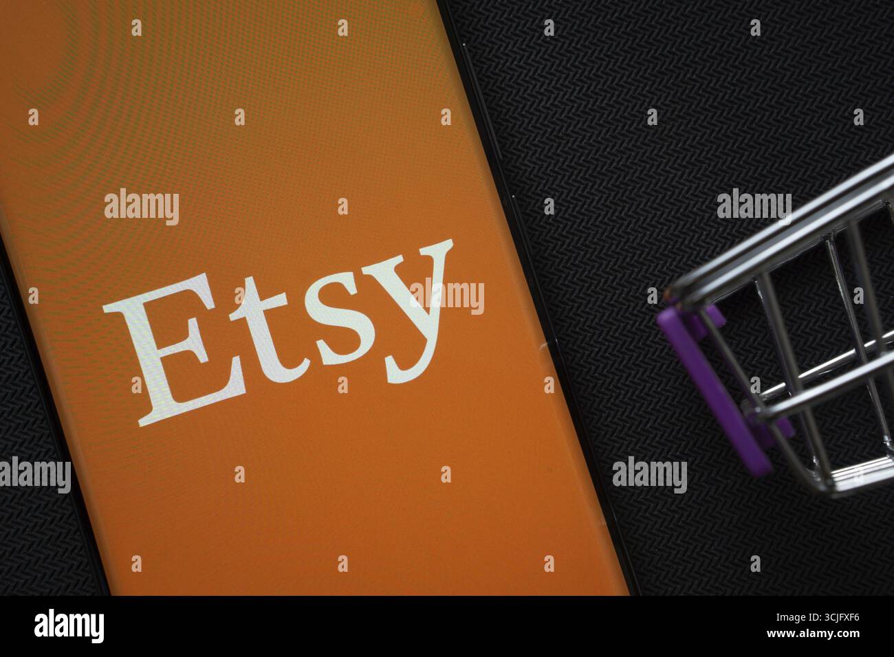 Dhaka, Bangladesch, 03. Juli 2025: Ein Smartphone mit dem Etsy-Logo neben einem Miniatur-Einkaufswagen auf einem Hintergrund Stockfoto
