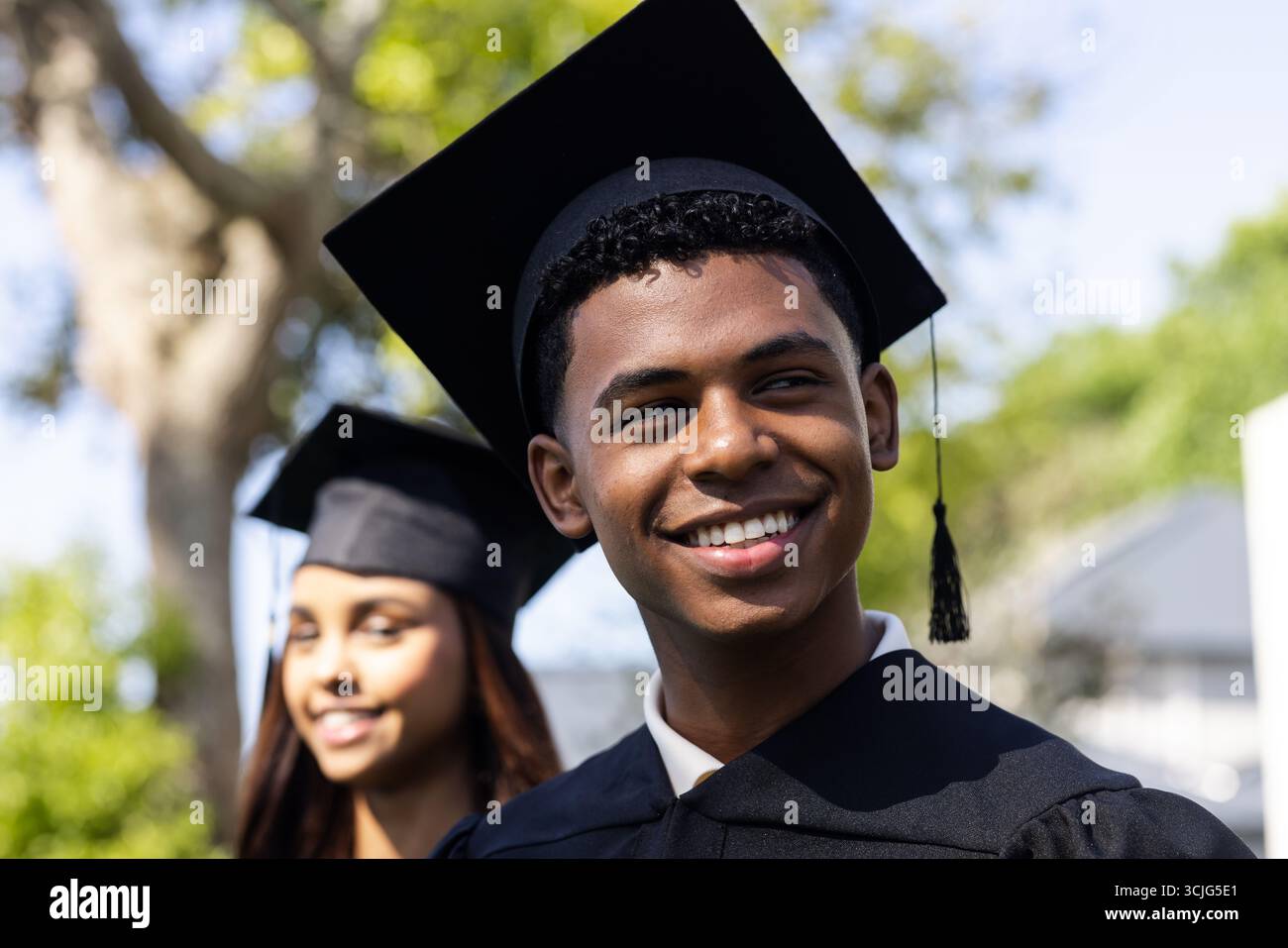 Abschlussschüler in Mütze und Kleid feiert akademische Leistungen im Freien, lächelnd Stockfoto