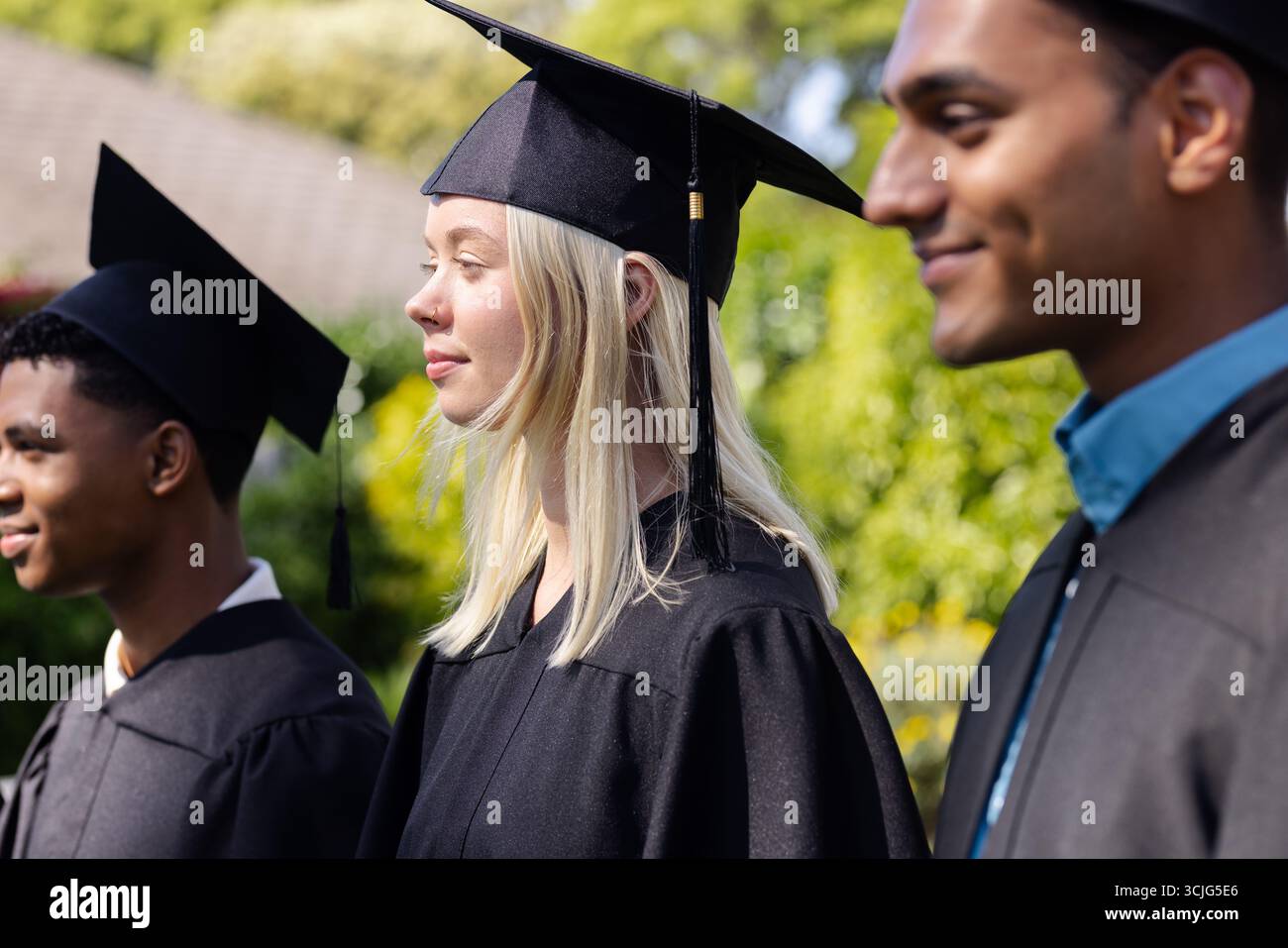 Absolventen in Mützen und Kleidern lächeln im Freien und feiern akademische Leistungen Stockfoto