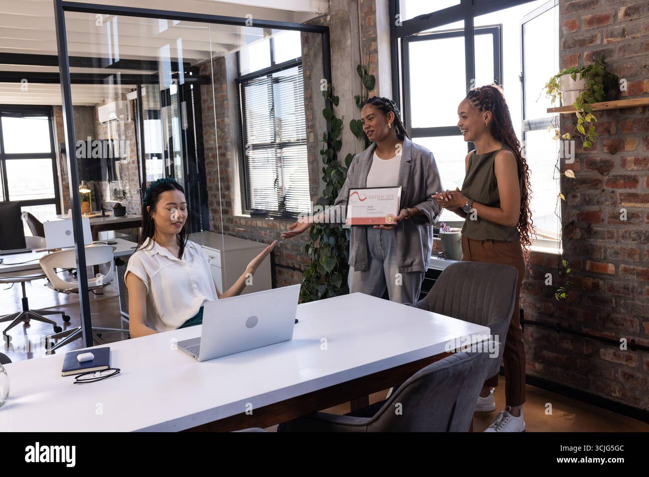Kollegen in modernen Büros überreichen Auszeichnung an lächelnde Frau am Schreibtisch Stockfoto