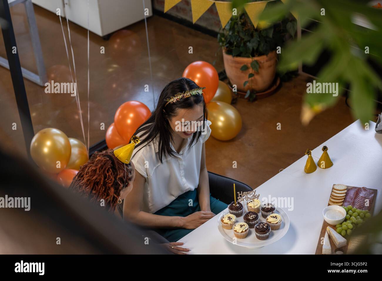 Feiert im Büro, lächelt eine Frau mit Cupcakes und Ballons auf dem Tisch Stockfoto