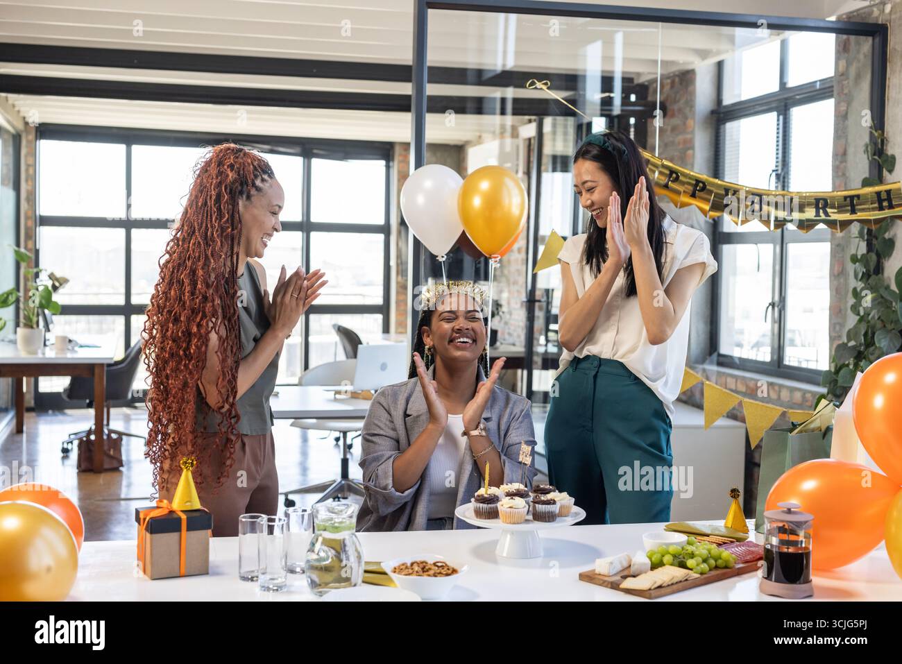 Kollegen feiern im Büro Geburtstag mit Ballons, Cupcakes und Lachen Stockfoto