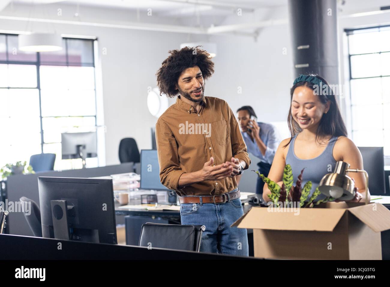Kollegen begrüßen neues Teammitglied beim Auspacken der Verpackung an einem modernen Arbeitsplatz Stockfoto