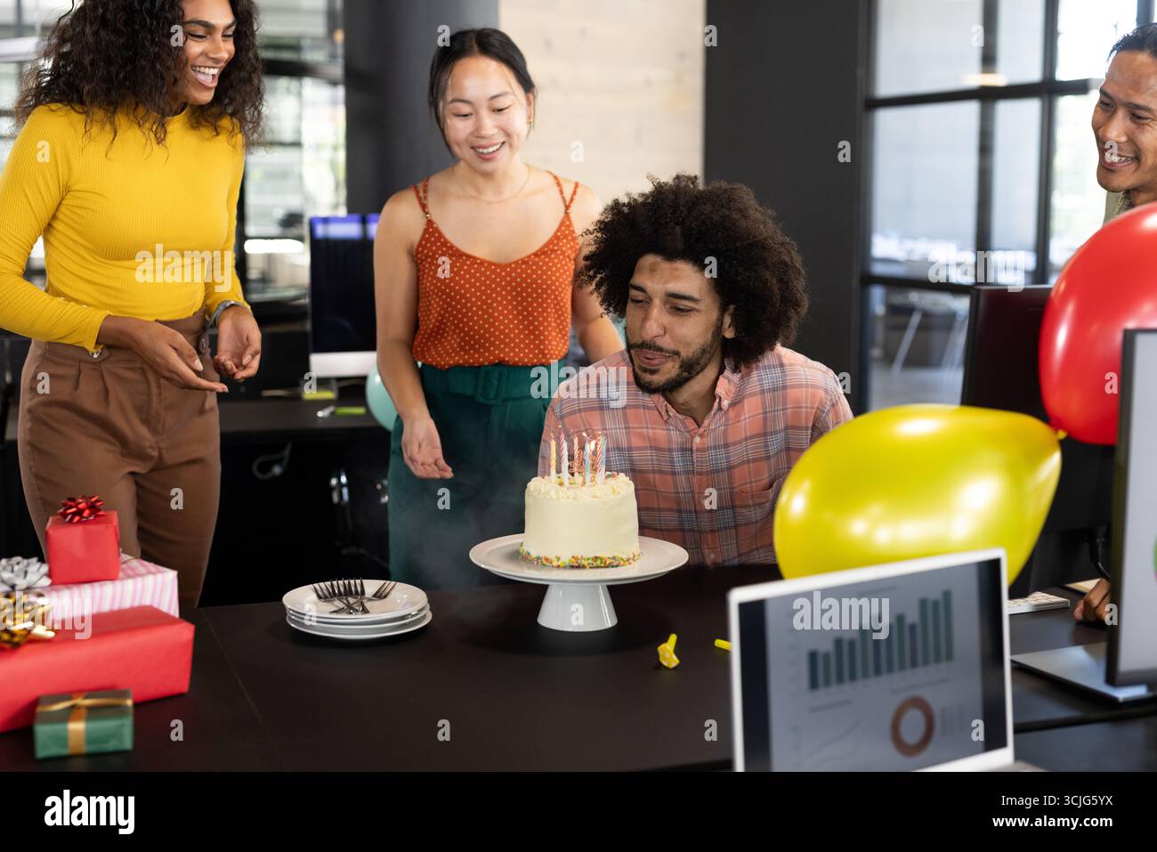Im Büro feiern wir Geburtstag, verschiedene Kollegen lächeln mit Kerzen um den Kuchen Stockfoto