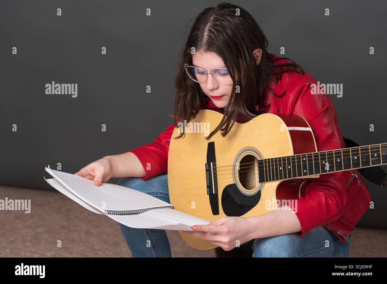 Die Musikerin untersucht sorgfältig Noten, während sie Gitarre hält. Ihr Gesichtsausdruck deutet darauf hin, dass sie sich intensiv auf ihre Aufgabe konzentriert Stockfoto
