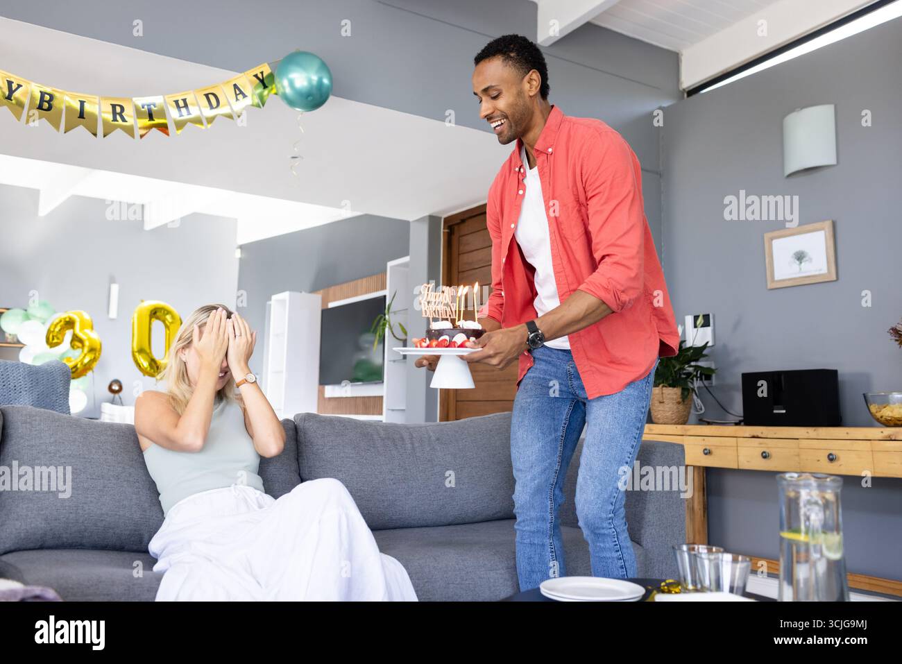 Mann überrascht Frau mit Geburtstagskuchen zu Hause, die einen freudigen Feiertag schaffen Stockfoto