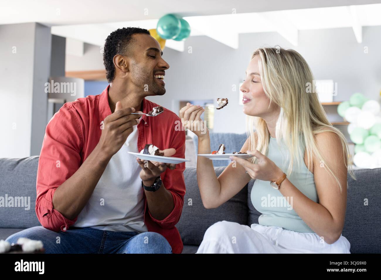 Paare genießen Kuchen zusammen auf dem Sofa und feiern fröhliche Momente zu Hause Stockfoto