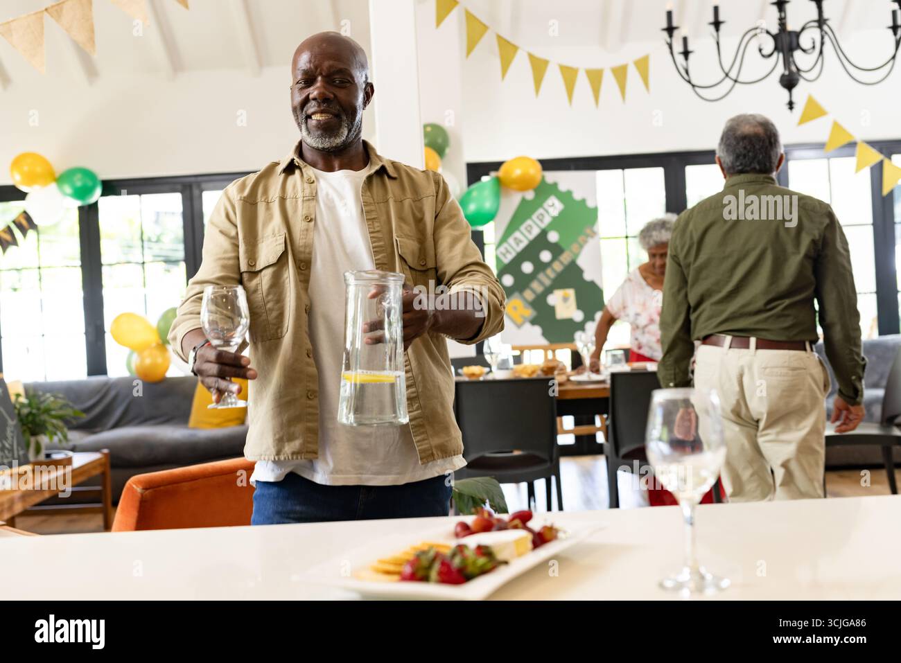 Mann serviert Getränke bei festlichen Familientreffen, lächelt und genießt die Feier Stockfoto