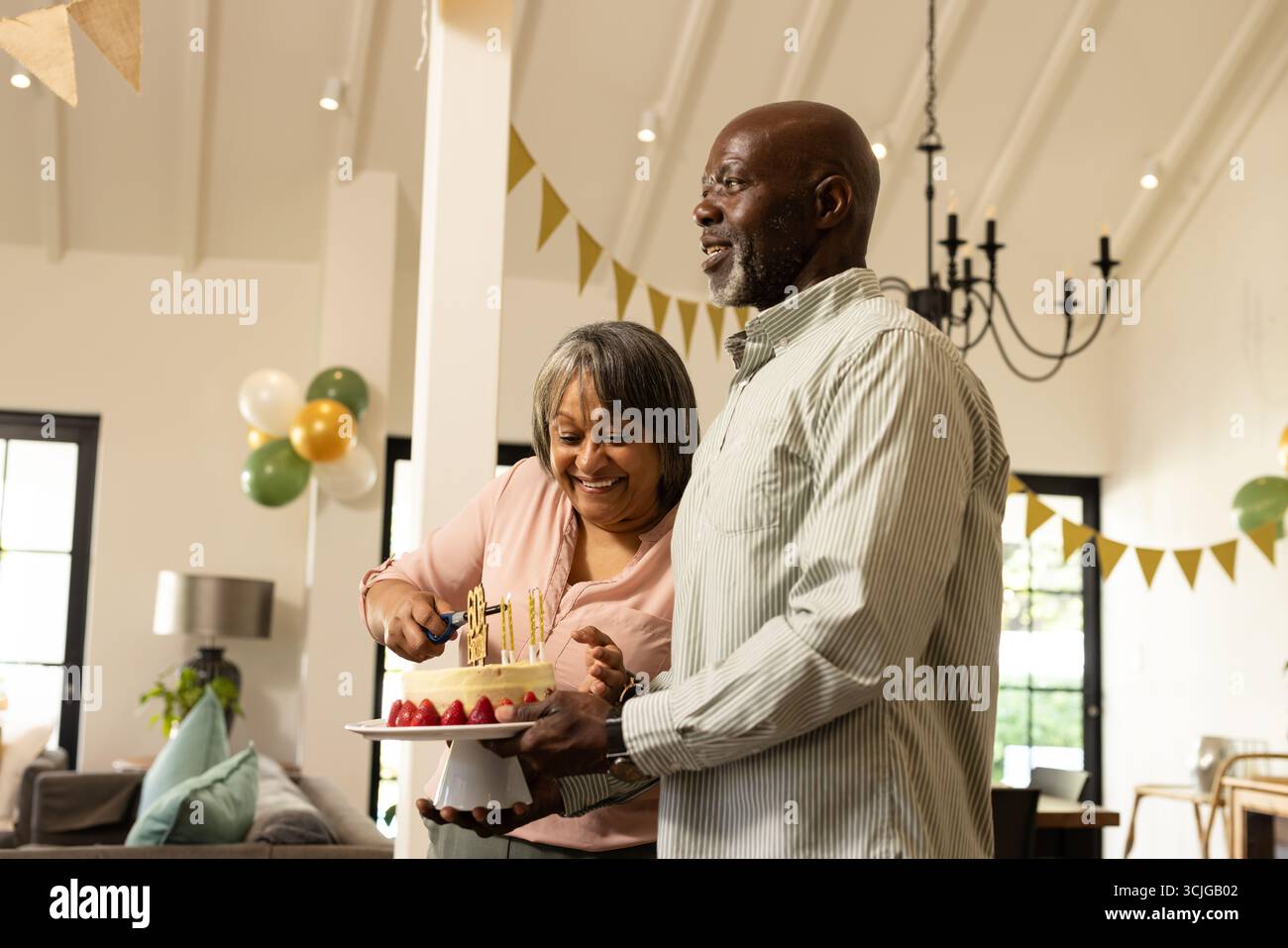 Lächelndes Paar schneidet während der festlichen Feier zu Hause Geburtstagskuchen Stockfoto