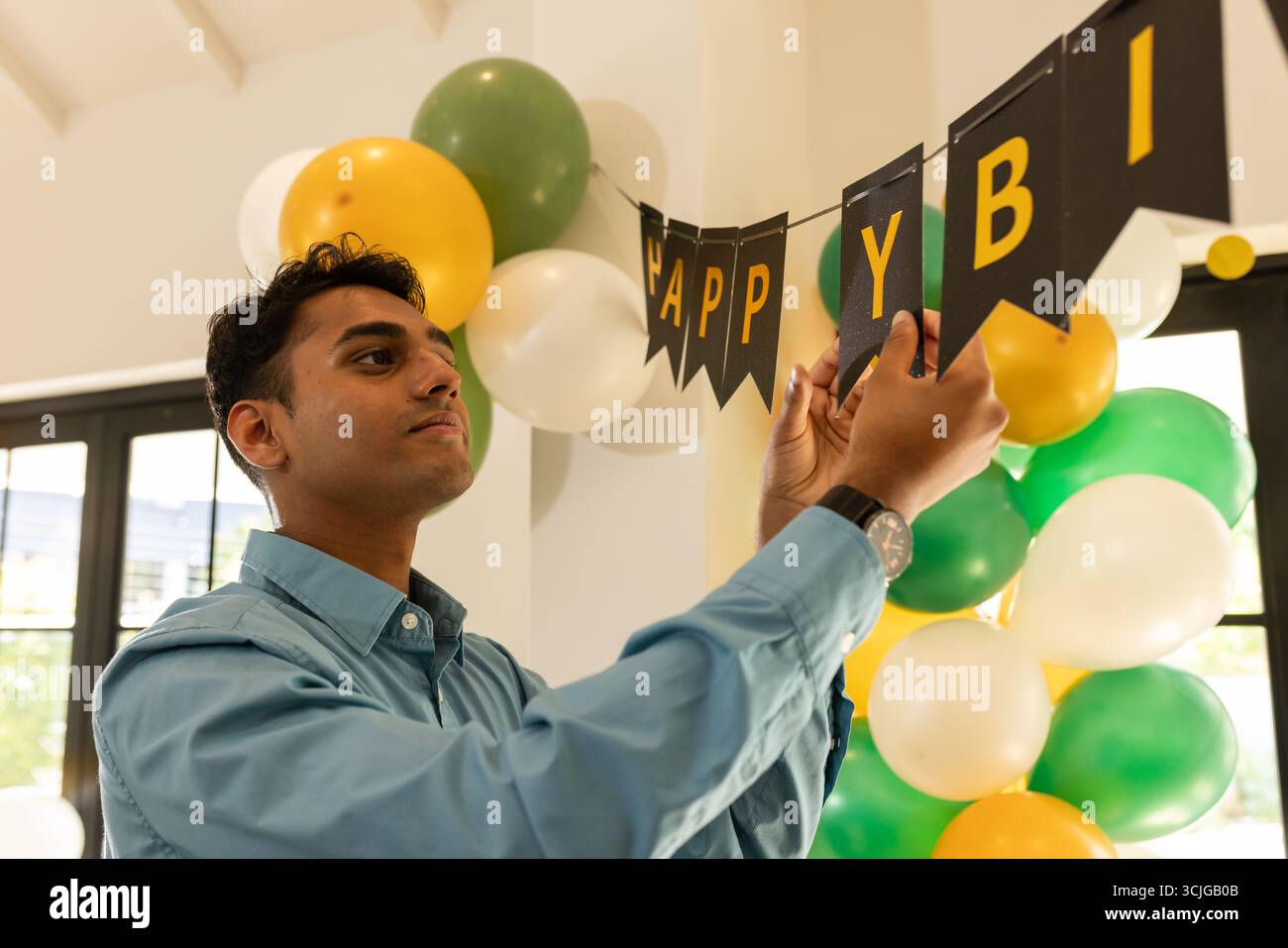 Mann dekoriert mit Geburtstagsbanner und Ballons, bereitet sich auf die Feier zu Hause vor Stockfoto