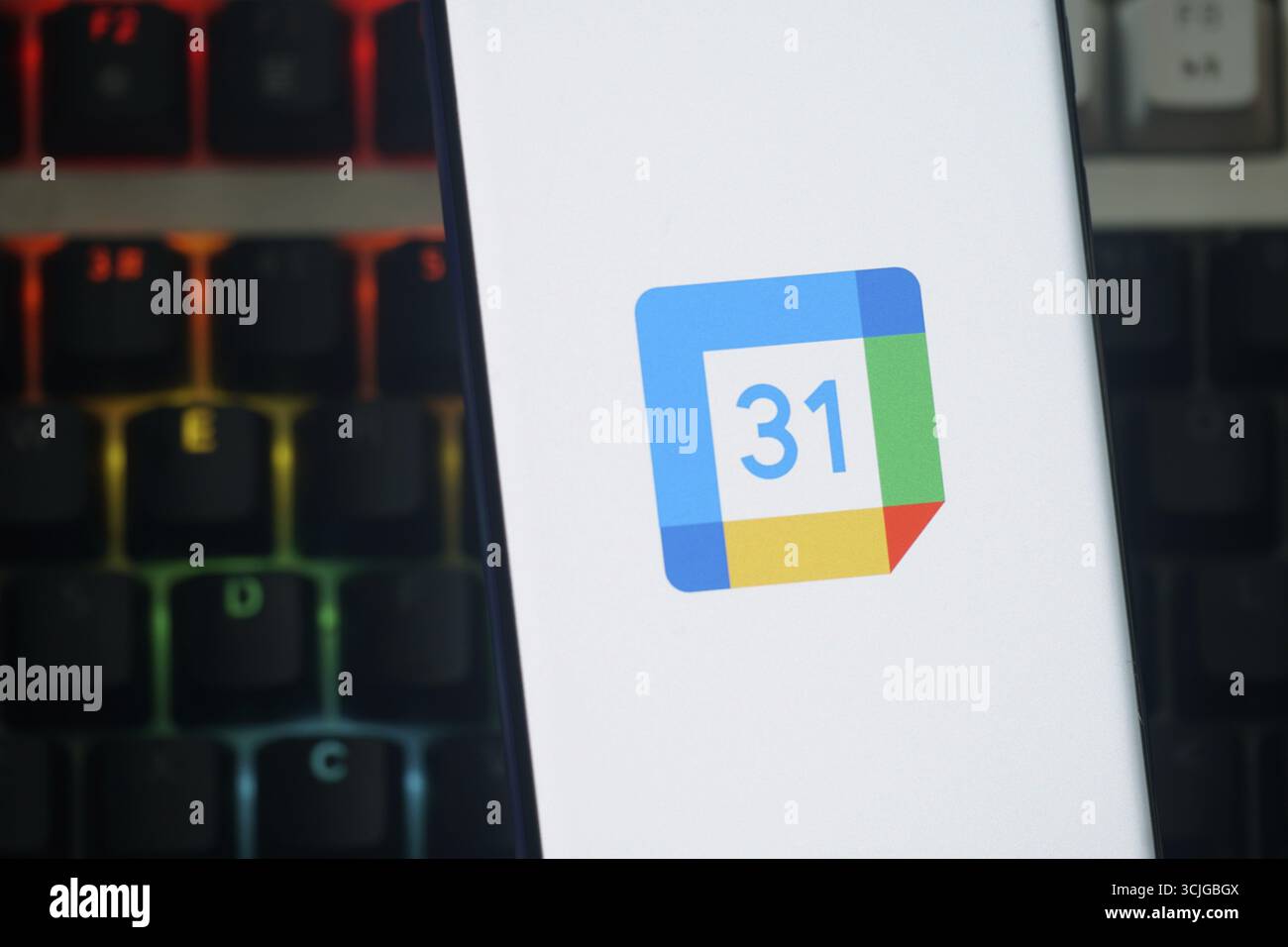 Smartphone-Display mit Google Kalender-Logo und farbenfroher hintergrundbeleuchteter Tastatur Stockfoto