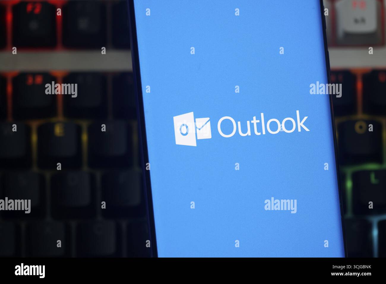 Outlook-Logo auf einem Smartphone mit blauem Hintergrund vor einer Tastatur Stockfoto