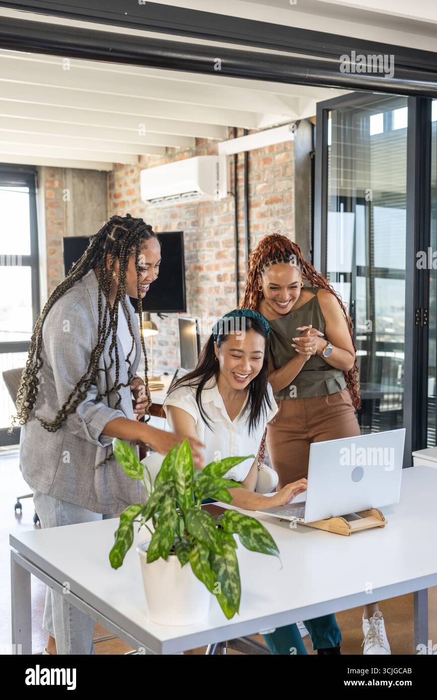 Vielseitiges Team, das Erfolg im Büro feiert, lächelt und sich ein Notebook anschaut Stockfoto