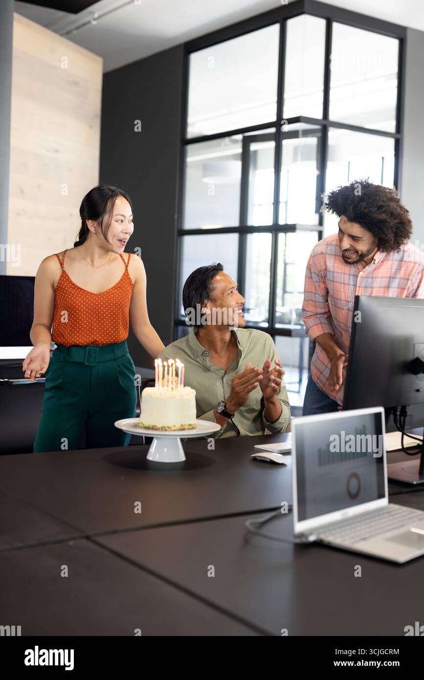 Im Büro feiern wir Geburtstag, verschiedene Kollegen lächeln mit Kerzen um den Kuchen Stockfoto