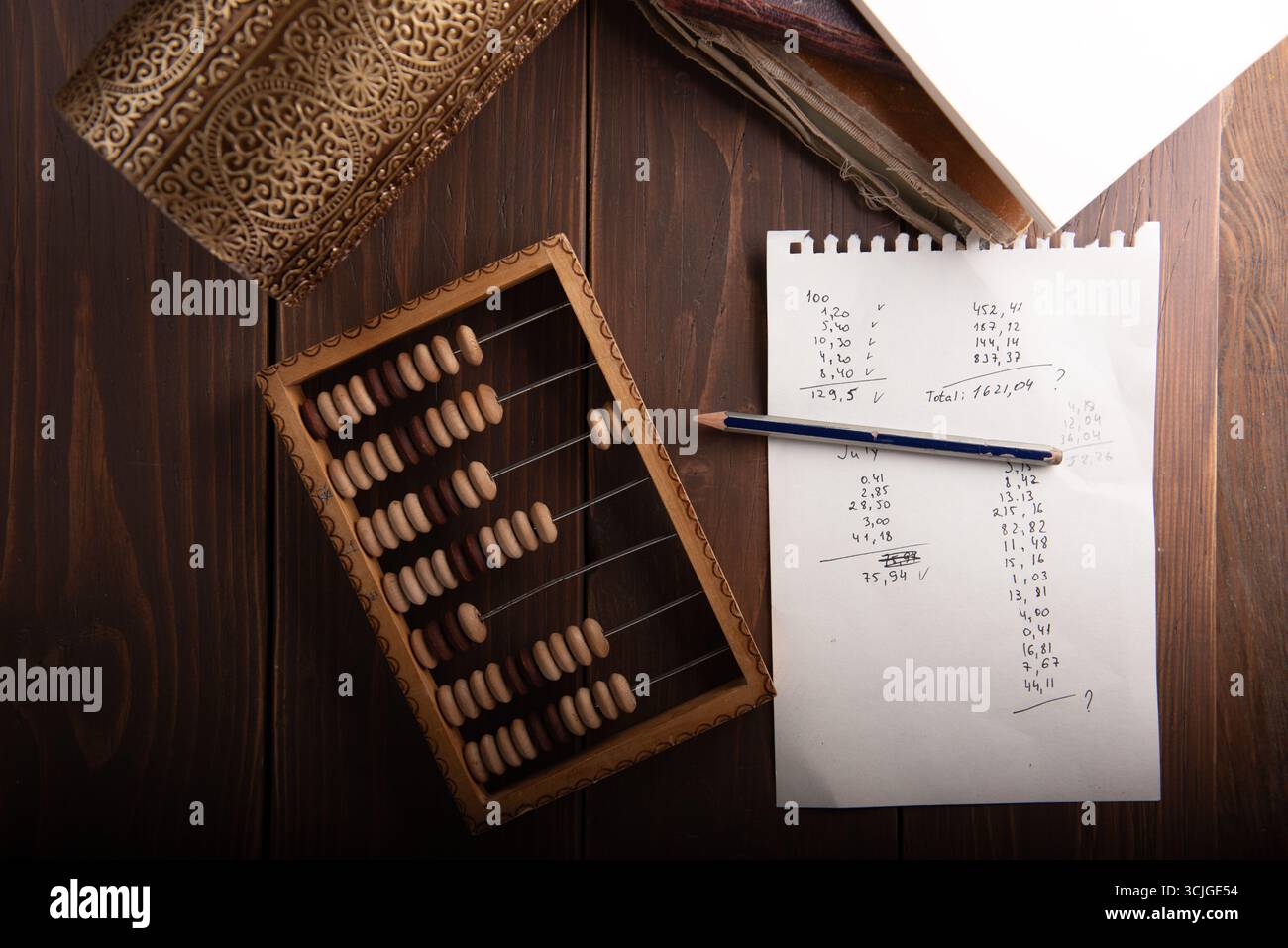 Der traditionelle hölzerne Abacus liegt auf einem rustikalen Tisch neben einem Notizblock mit handschriftlichen Berechnungen und einem Bleistift, der mathematische Praktiken und zeigt Stockfoto