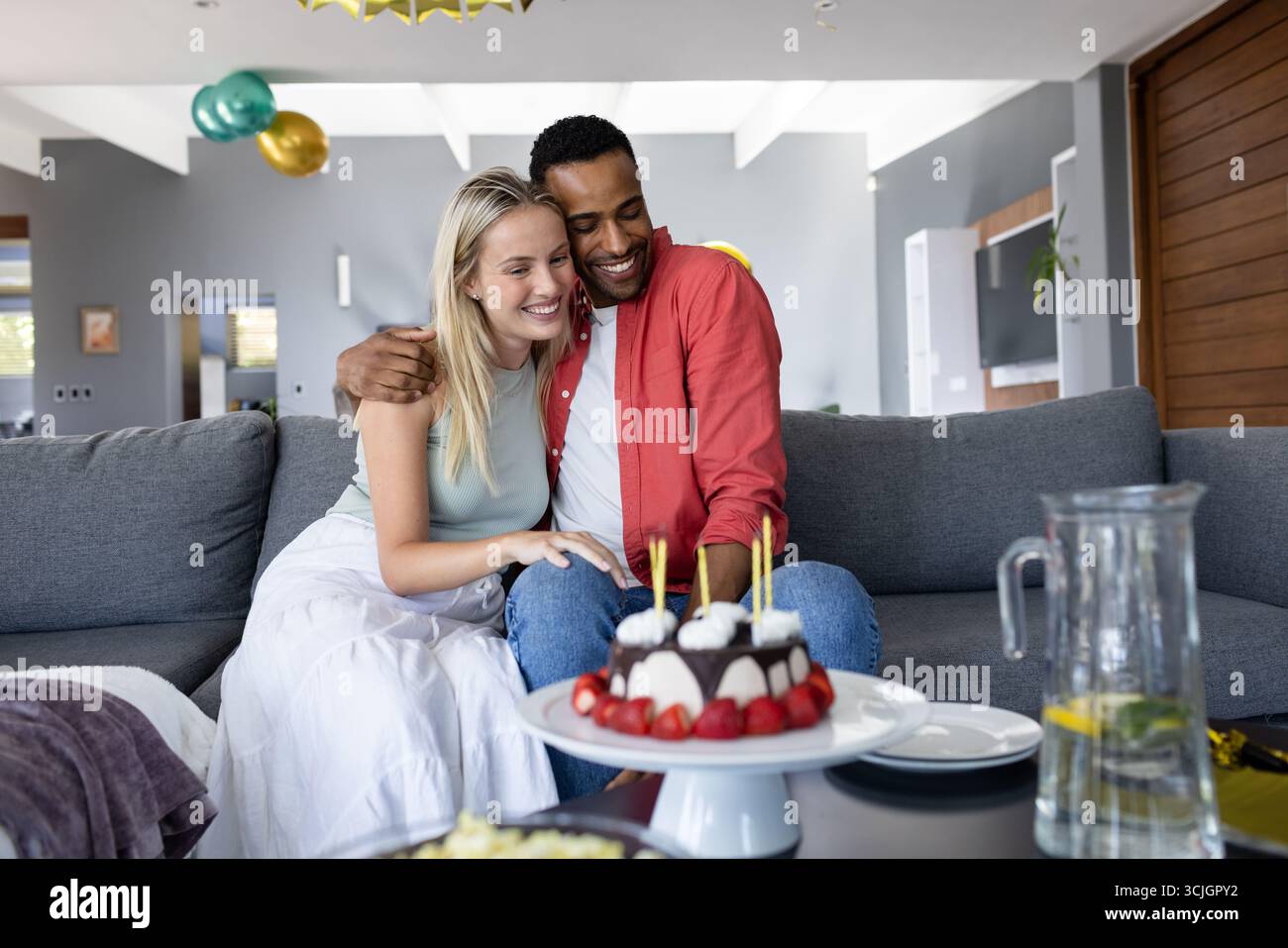 Ein Paar feiert zu Hause Geburtstag und lächelt mit Kuchen und Kerzen auf dem Tisch Stockfoto