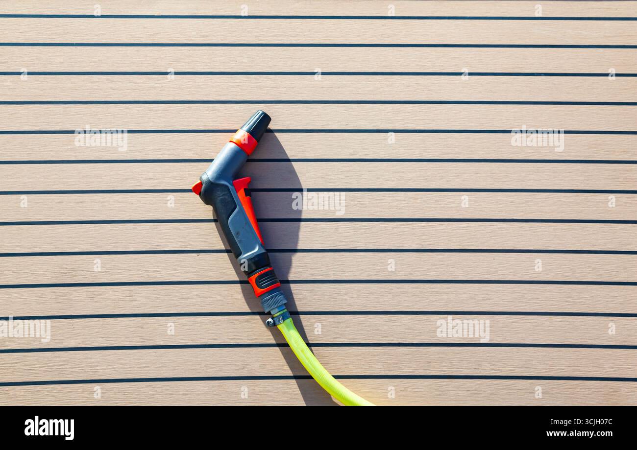 Ein Schlauch mit einer Pistole zum Waschen von Yachten auf dem Teakdeck einer Yacht, Draufsicht. Stockfoto