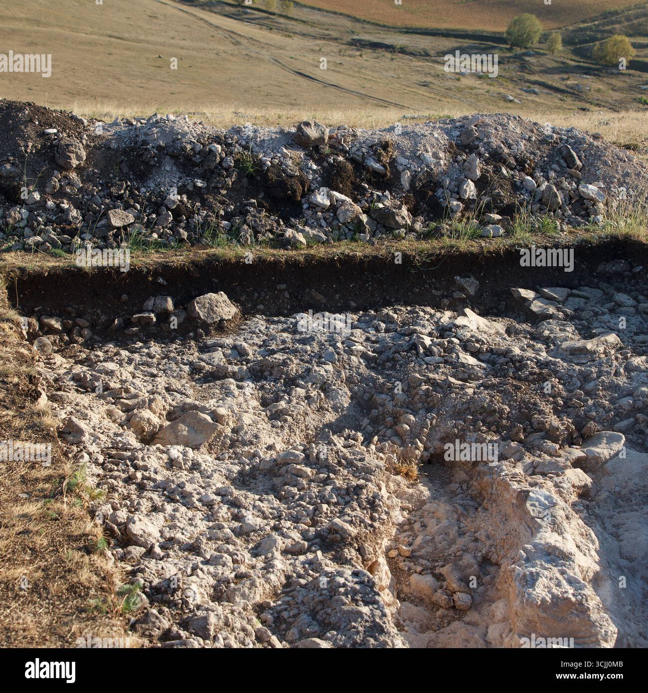 Freiliegende archäologische Grabstätte mit Bodenschichten und kalkhaltiger Oberfläche, Tageslichtfoto, natürliches Gelände, Konzept der Ausgrabung aus der Antike Stockfoto