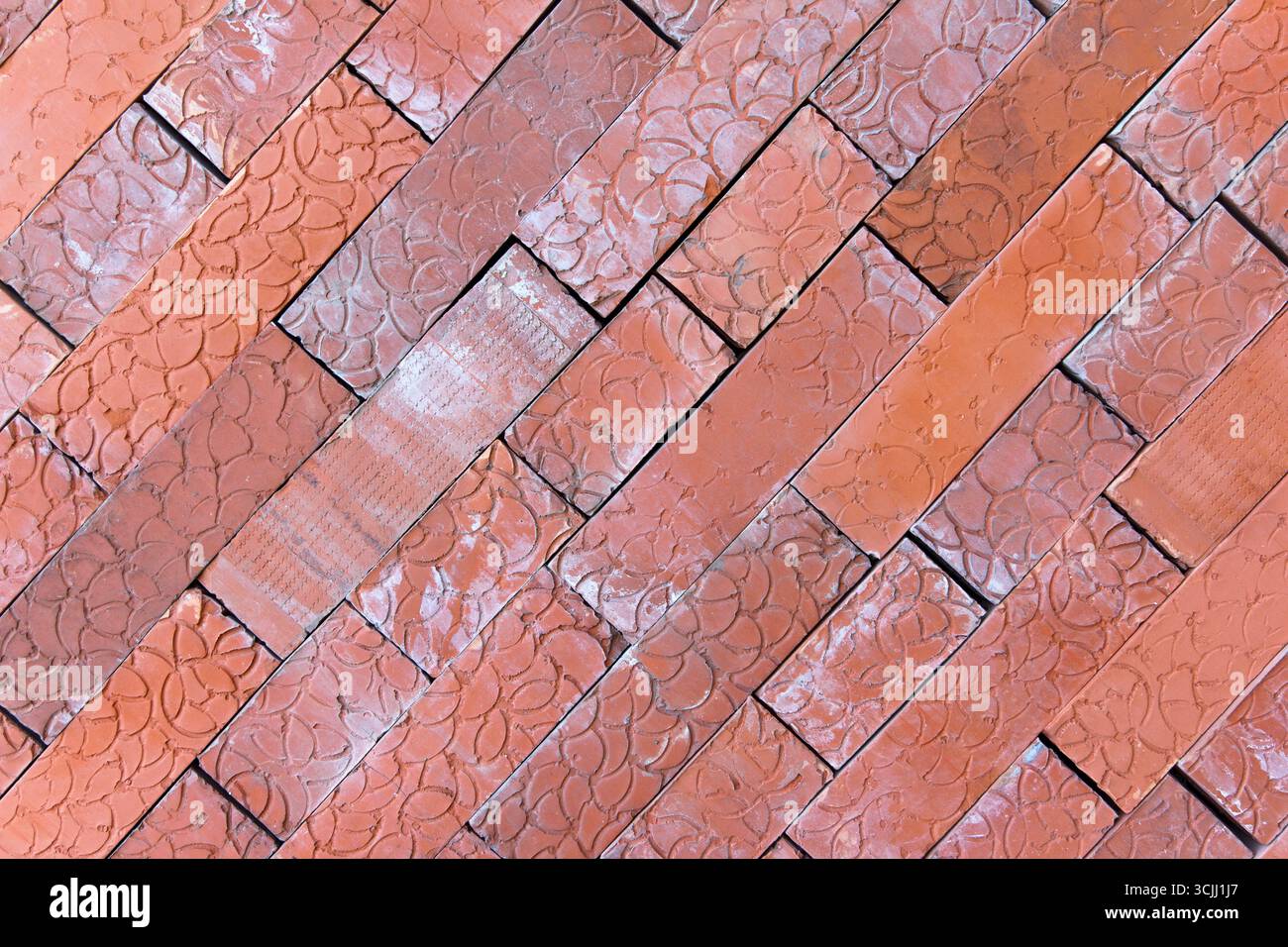 Nahaufnahme eines Fischgrätenmusters aus roten Ziegeln. Die Ziegel sind diagonal angeordnet und zeigen ihre Textur und Farbvarianten Stockfoto