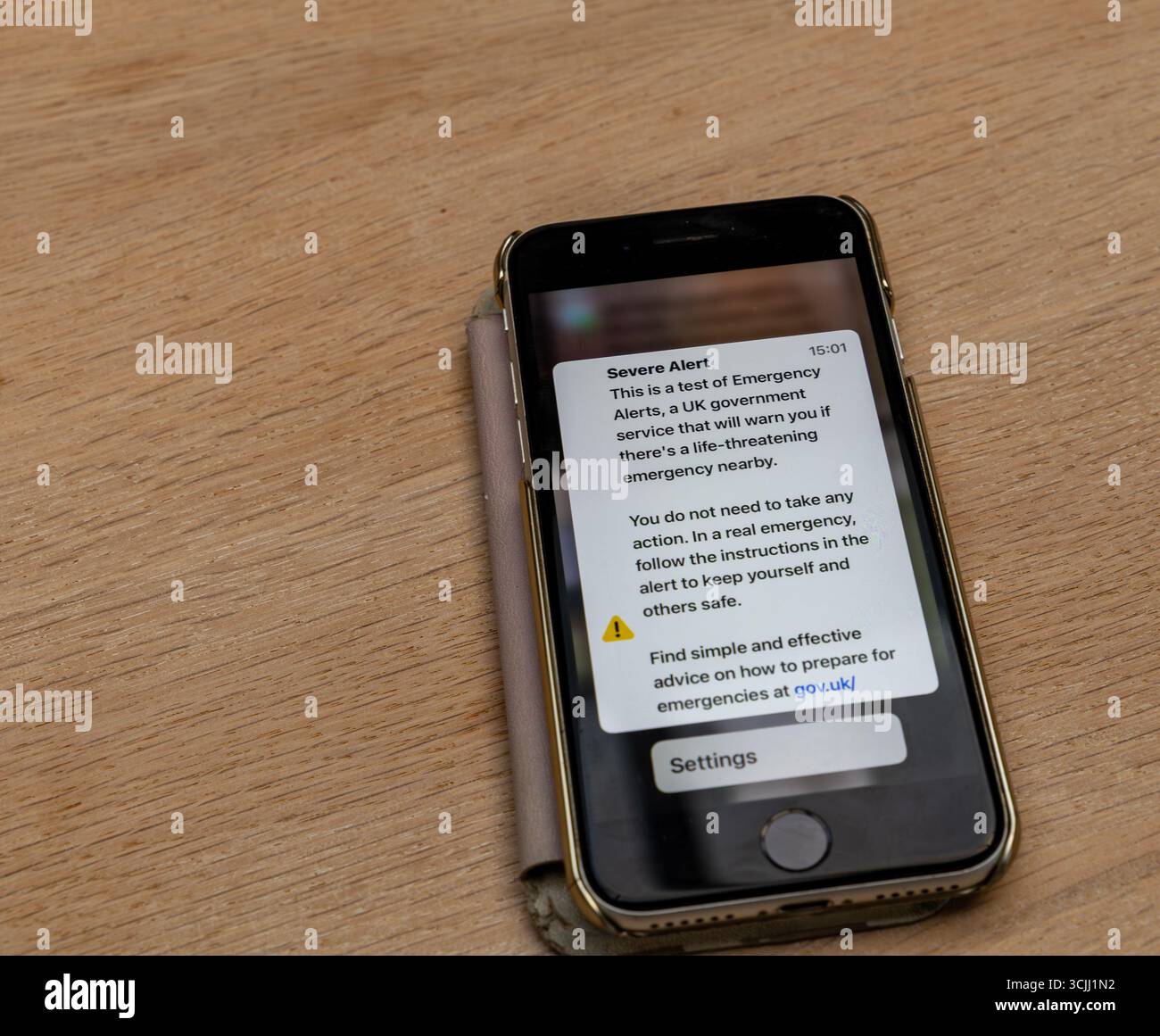 Smartphone, das die Benachrichtigung über Notfalltests der britischen Regierung auf hölzernen Oberflächen anzeigt, die über lebensbedrohliche Situationen warnen Stockfoto