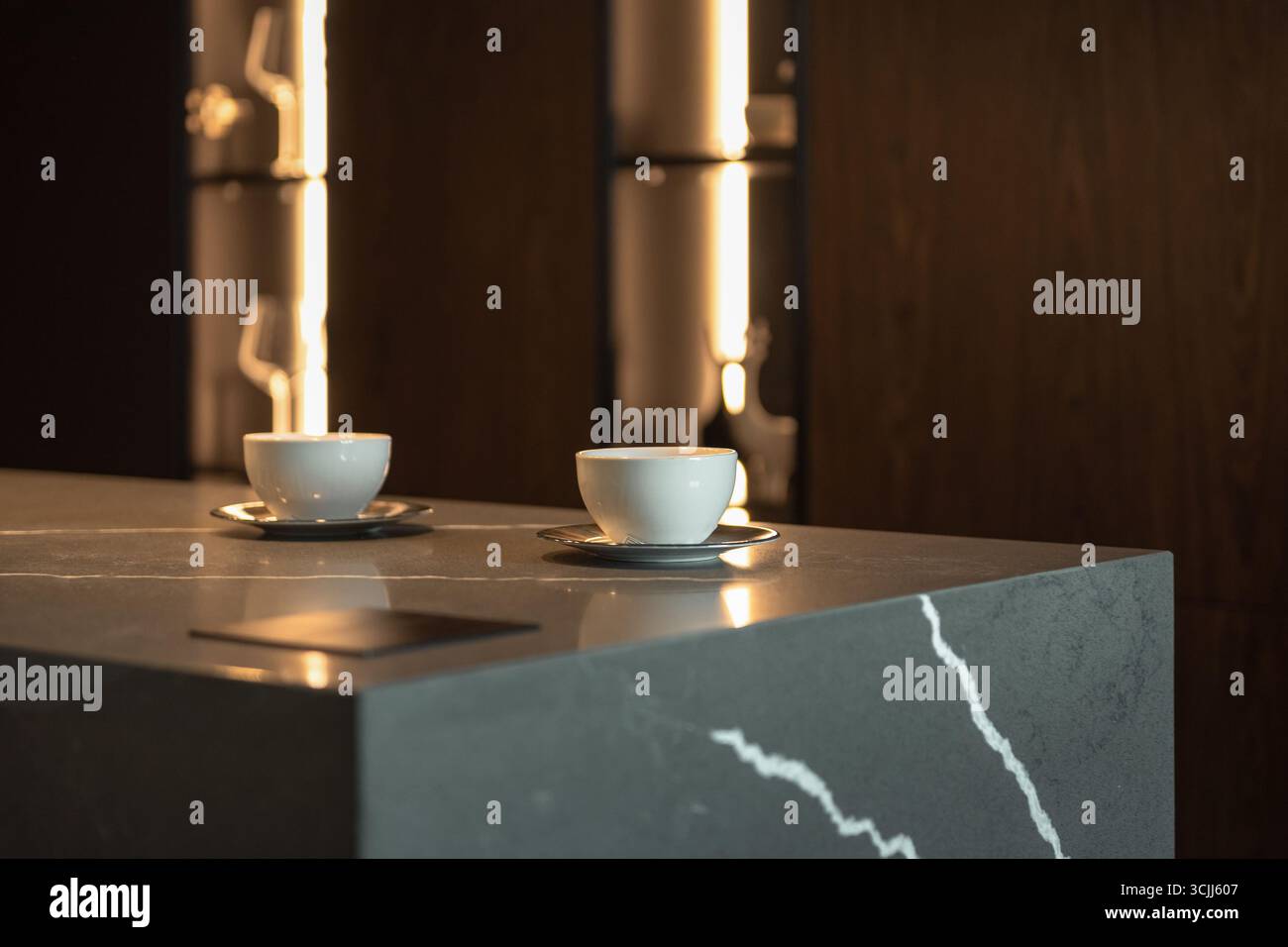 Zwei Tassen Kaffee auf einem Tisch. Zwei kleine weiße Tassen auf einem grauen Steintisch, warme Beleuchtung im Hintergrund. Stockfoto