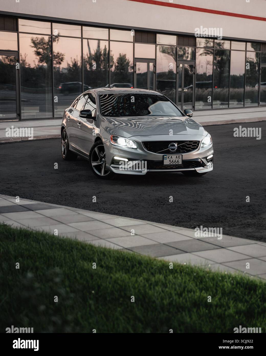 Silver Volvo S60 in einer Straße in der Nähe eines modernen Glasgebäudes. Dreiviertelansicht der schwedischen Sportlimousine, die auf der Außenseite der Straßenkurve geparkt ist. Stockfoto