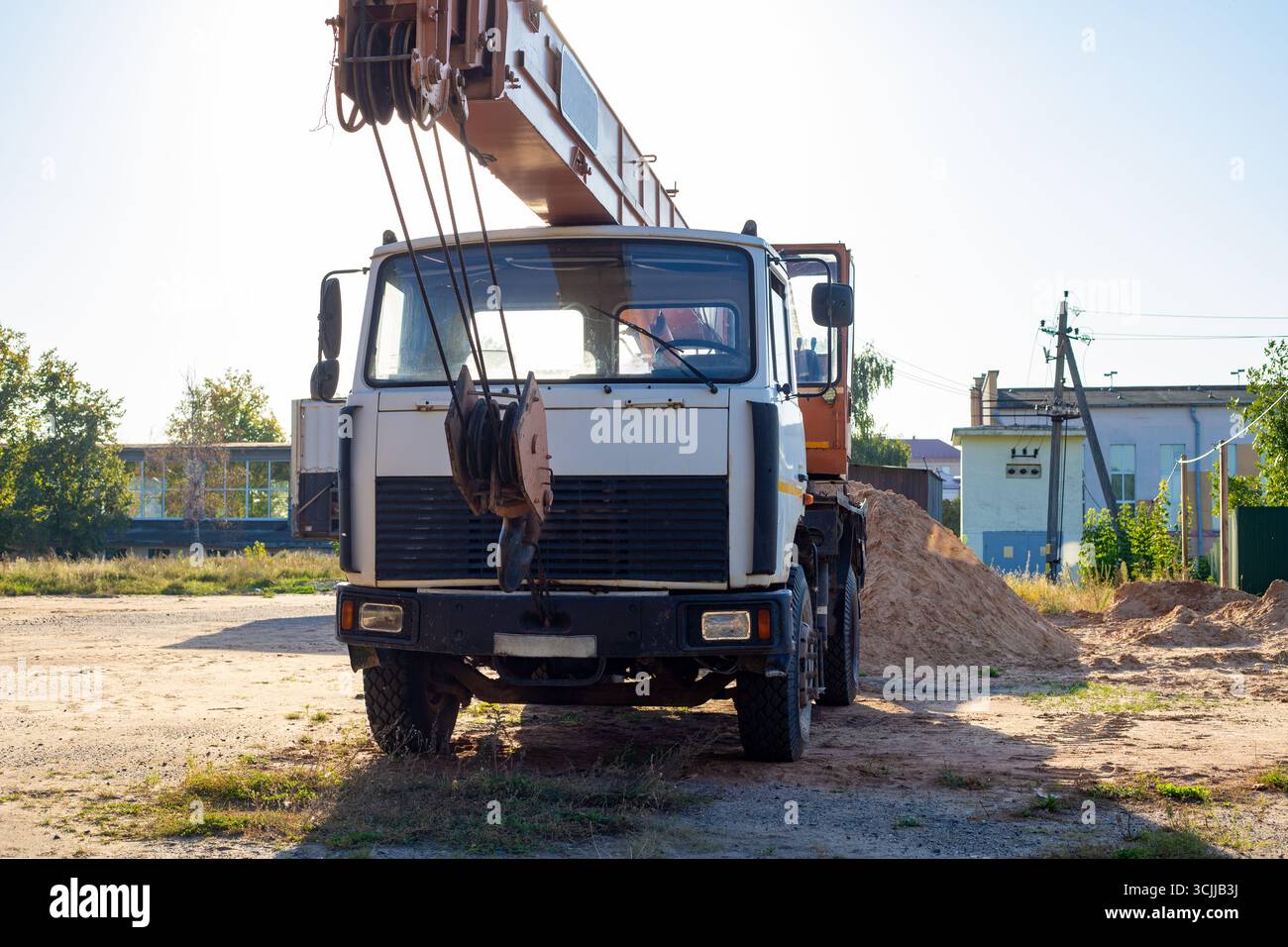 Alter Mobilkran auf einer Baustelle vor dem Hintergrund eines Zauns und eines Sandhaufens am Abend nach der Arbeit. Vorderansicht Stockfoto