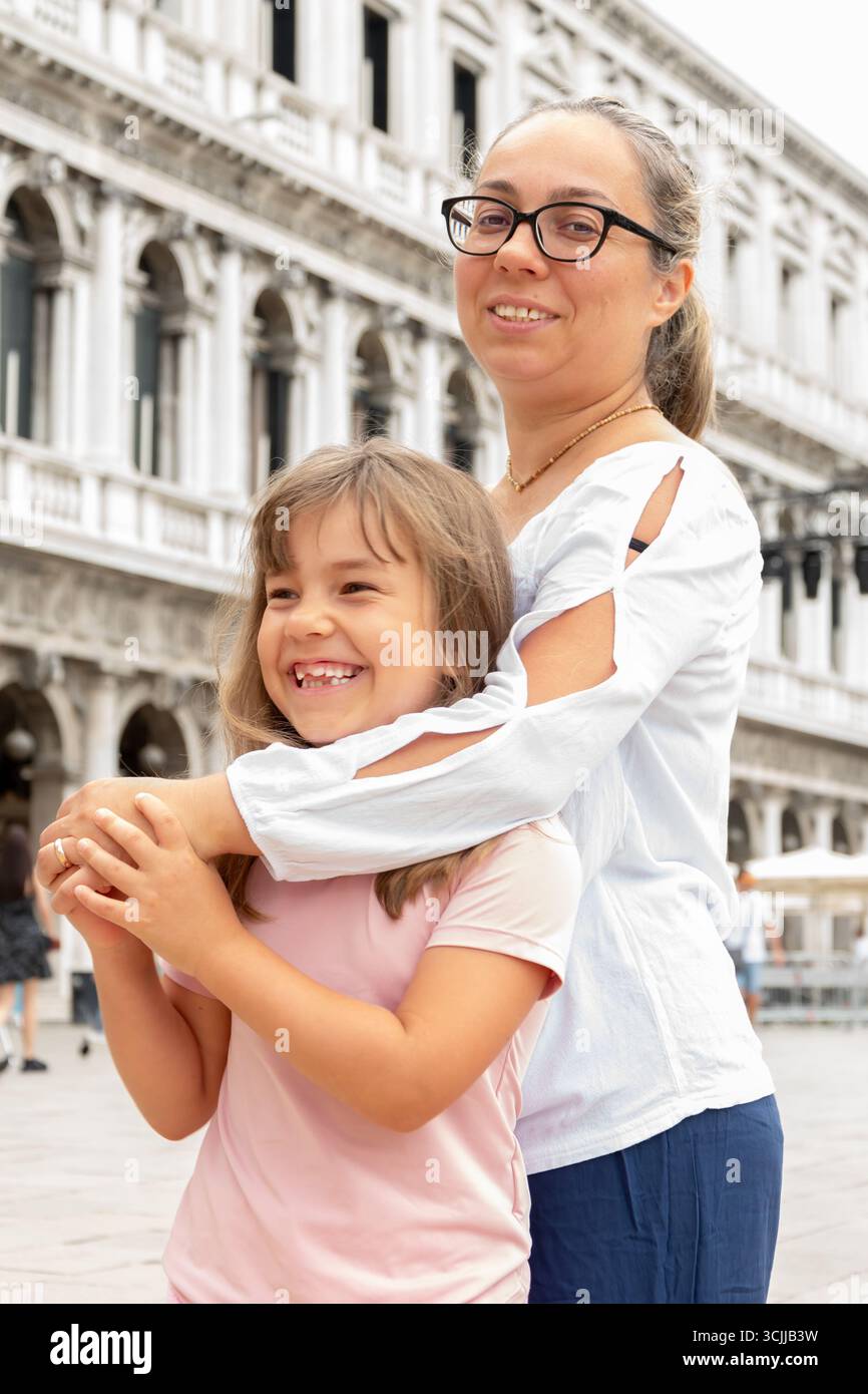 Eine Frau umarmt ein lächelndes Mädchen auf dem Markusplatz in Venedig Stockfoto