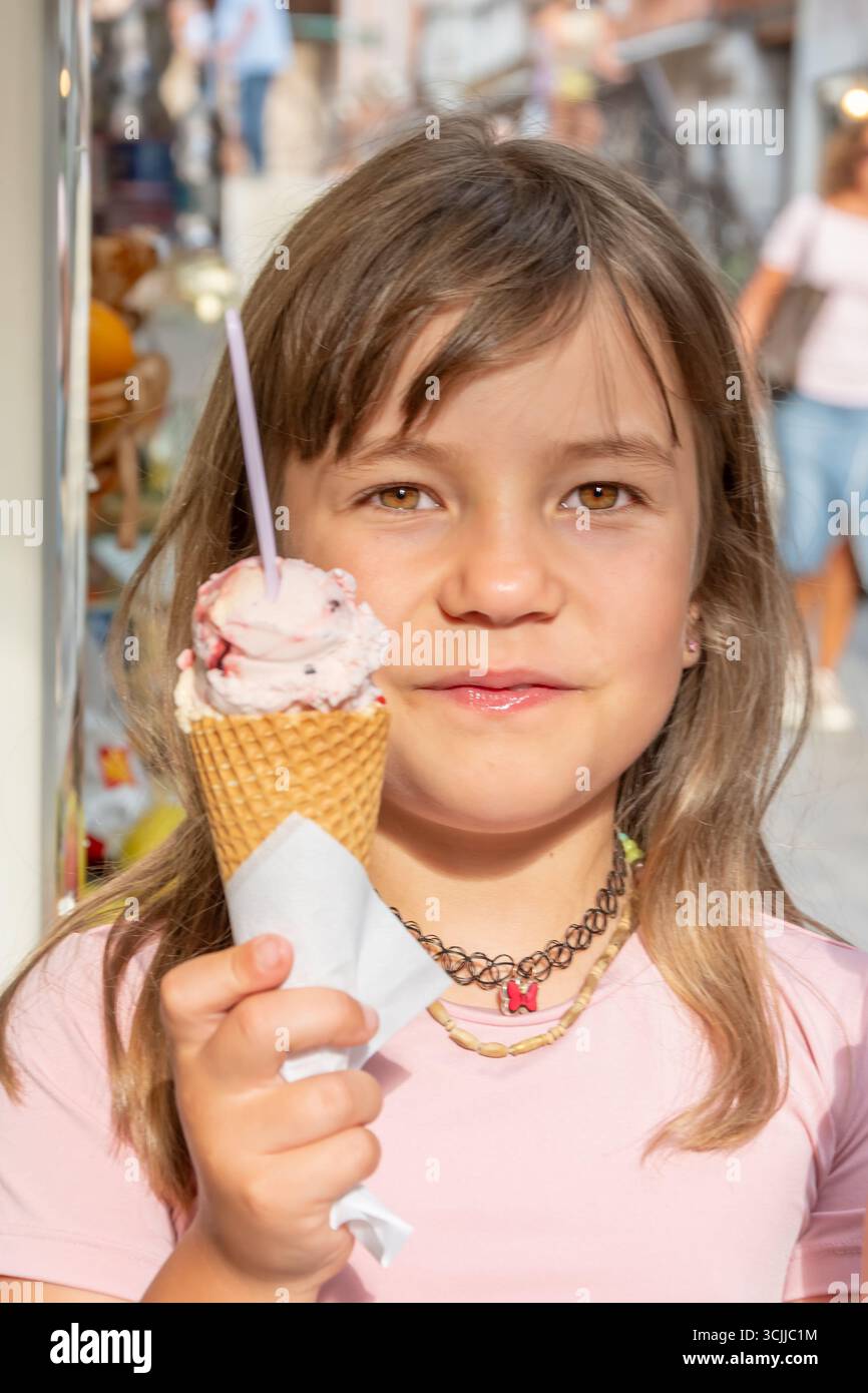 Straßenporträt eines 8-jährigen Mädchens, das an einem sonnigen Sommertag eine Eiskugel hält Stockfoto