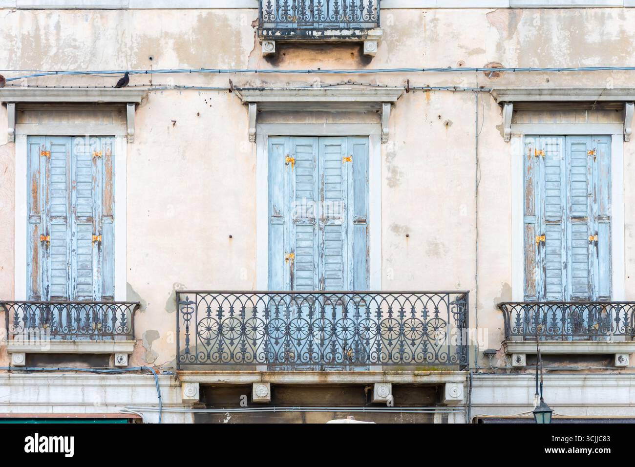 Die fassade des Hauses mit Balkonen und blauen Fensterläden an den Fenstern, mit schmiedeeisernen Geländern und abblätterndem Putz Stockfoto