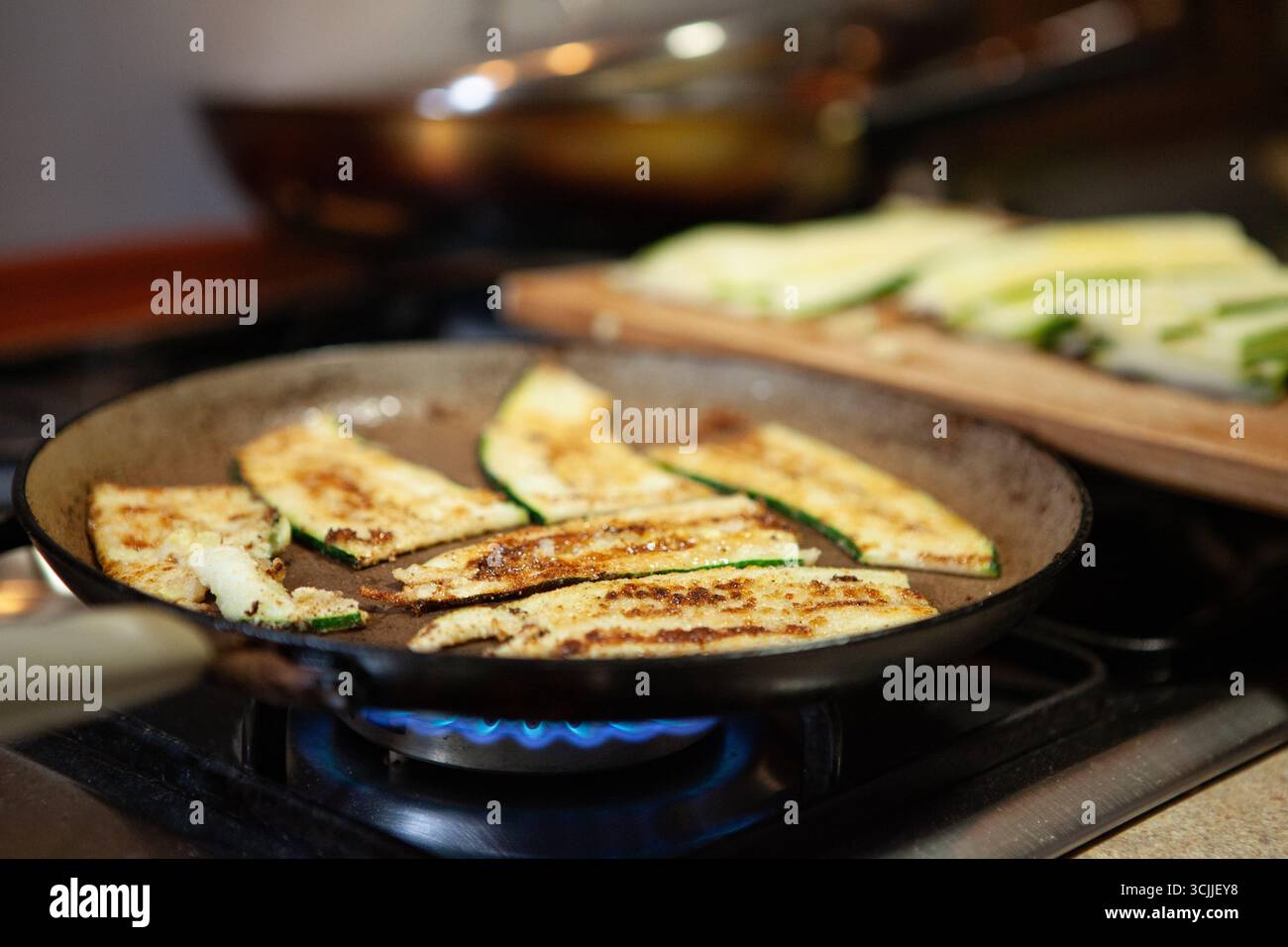 Goldbraune Zucchini-Scheiben, gegrillt auf einer Pfanne. Ein gesundes, hausgemachtes Gemüsegericht auf einem Gasherd. Stockfoto
