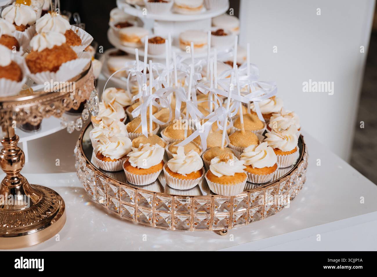 Luxuriöse Schokoriegel mit Cupcakes, Macarons und Desserts auf eleganten goldenen Tabletts Stockfoto