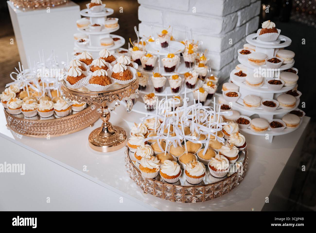 Luxuriöse Schokoriegel mit Cupcakes, Macarons und Desserts auf eleganten goldenen Tabletts Stockfoto