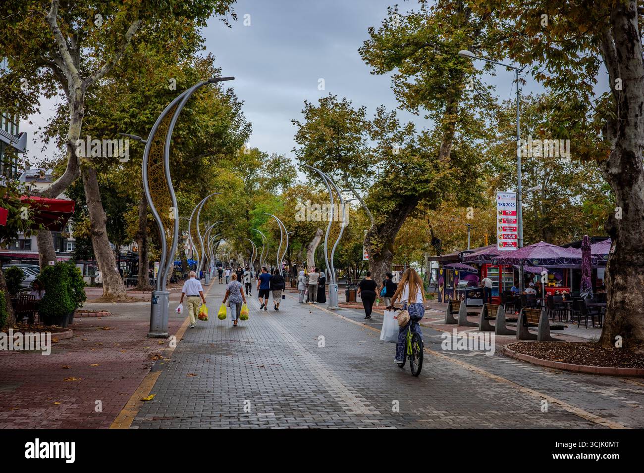 In Yalova, Türkei, spazieren und radeln die Menschen entlang einer von Bäumen gesäumten Fußgängerzone mit modernen Straßenlaternen und Cafés. Yalova, Provinz Yalova, Türkisch Stockfoto