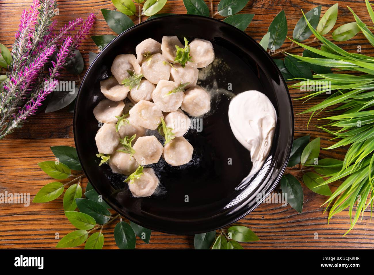 Ein Foto mit Pelmeni, einem traditionellen ukrainischen Knödel mit Fleischfüllung, präsentiert mit Sauerrahm und Kräutern für einen herzhaften Genuss. Stockfoto