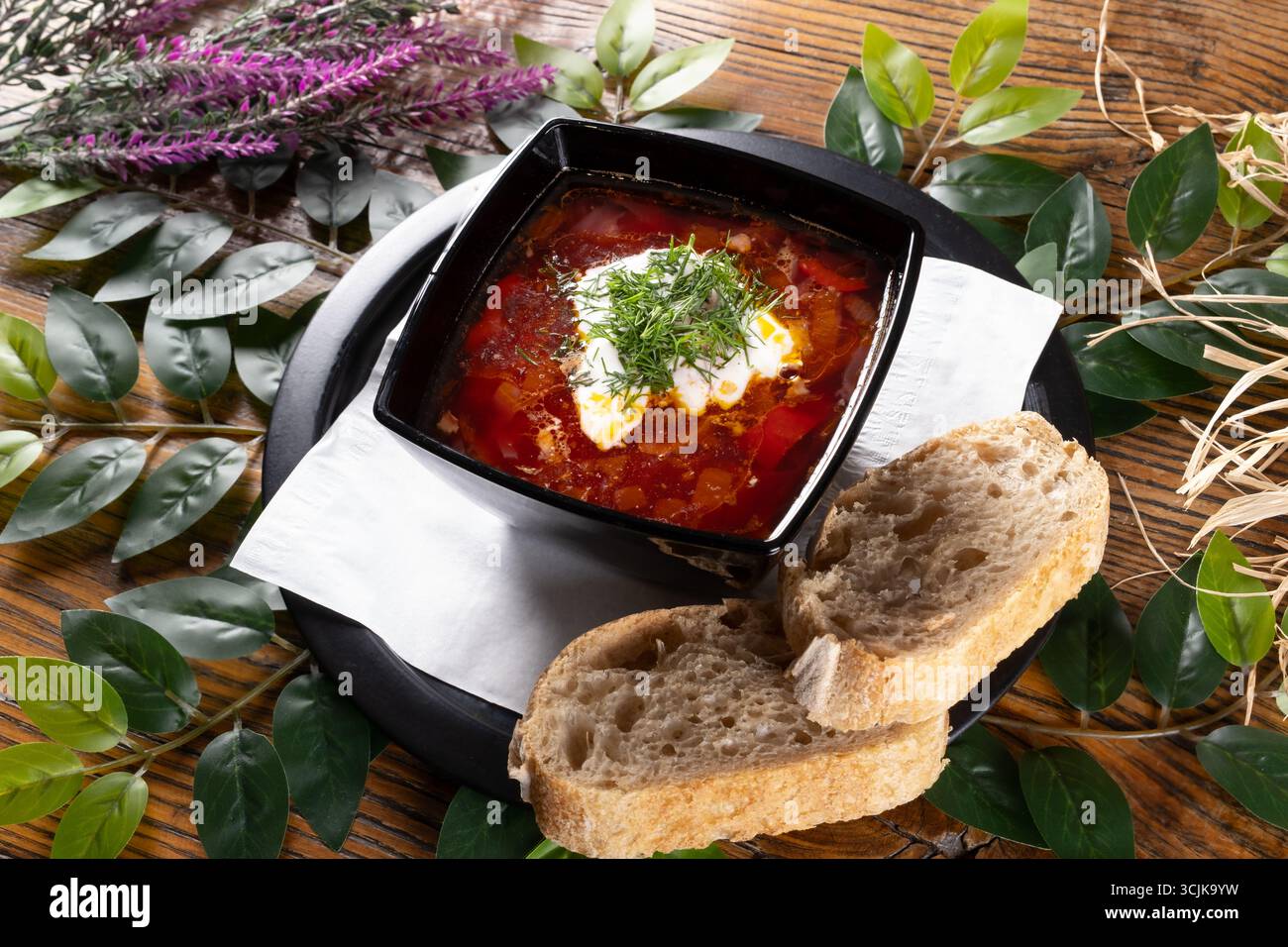 Ein Foto mit Borsch, einer traditionellen ukrainischen Rübensuppe, präsentiert in lebhaften Farben und serviert mit einem Klecks Sauerrahm und frischen Kräutern. Stockfoto
