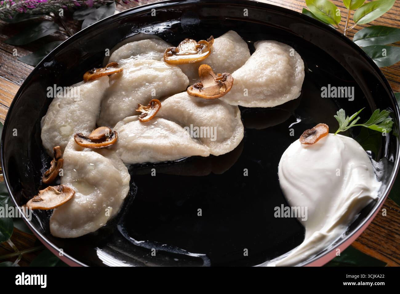 Ein Foto mit Vareniki, einem traditionellen ukrainischen Knödel, präsentiert mit einer herzhaften Füllung und serviert mit einem Klecks Sauerrahm und Kräutern Stockfoto