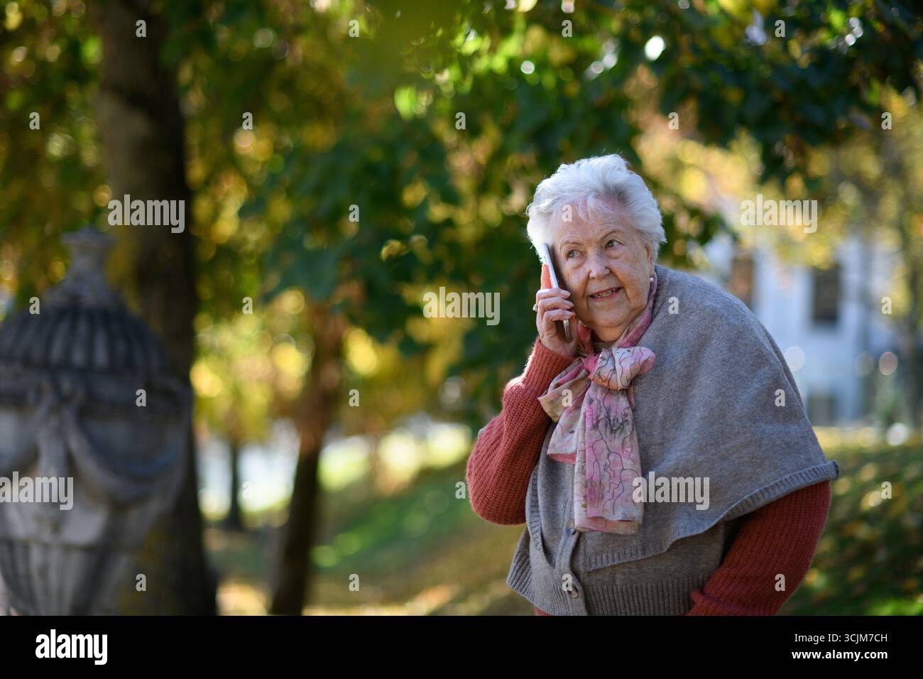 Eine ältere Frau im Park, die ein Smartphone hält und mit jemandem telefoniert. Stockfoto