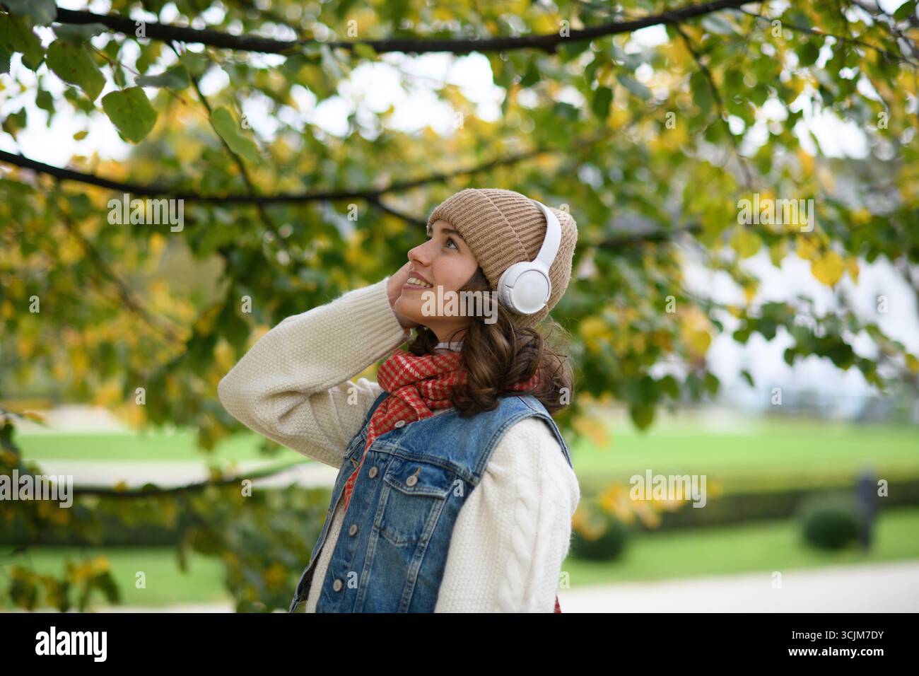 Schöne junge Frau, die im Herbstpark spaziert, Musik hört und einen friedlichen Moment für sich selbst genießt. Stockfoto