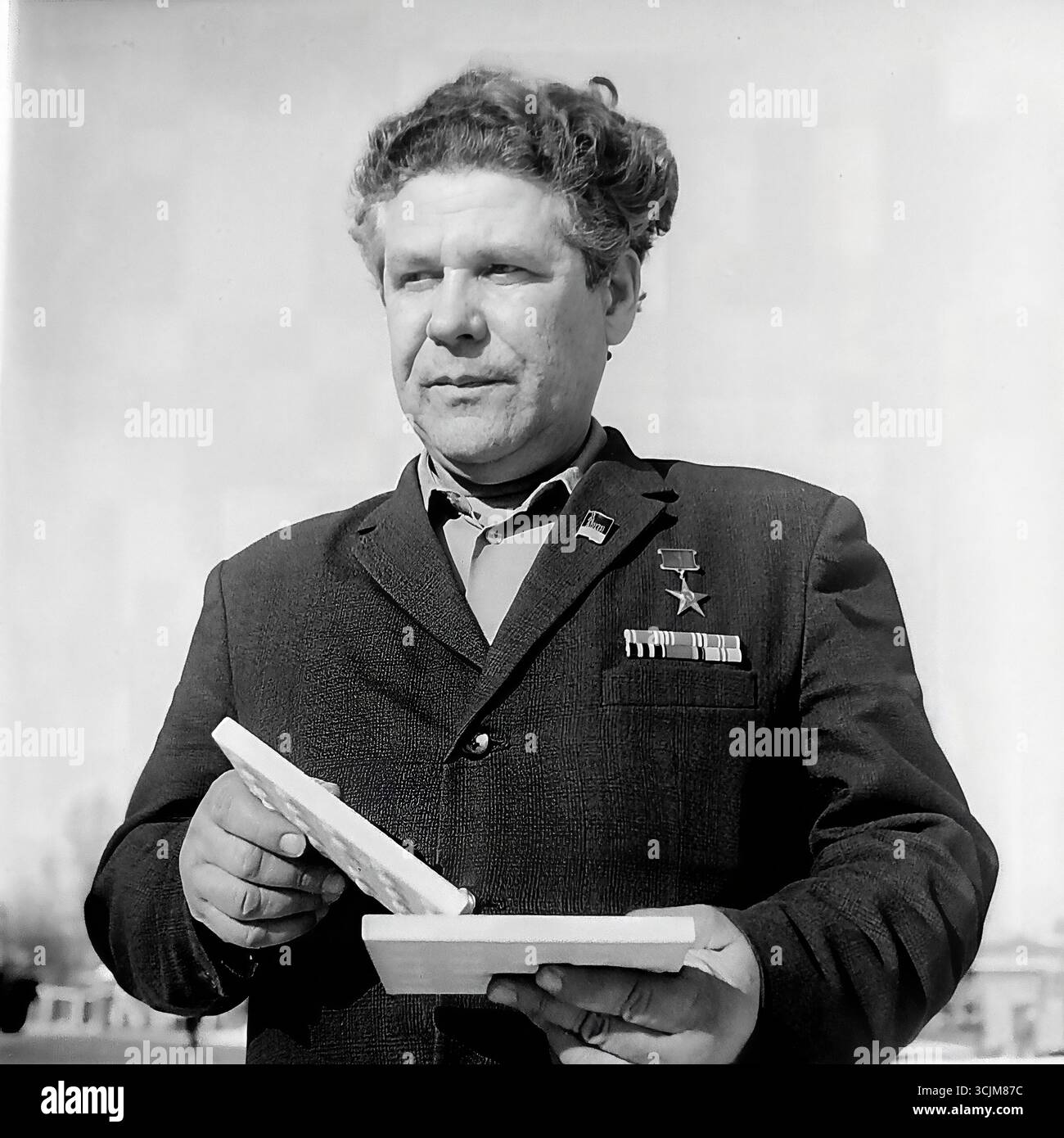 Ein Porträt eines Helden der Sozialistischen Arbeit vor seiner Hausfabrik in Slawjansk, 1976. Diese monumentale Aufnahme aus der Stagnation-Ära, die einen dekorierten Arbeitsveteranen mit Auszeichnungen auf der Brust einfängt, ist ein Symbol für die Verherrlichung der Arbeiterklasse, die höchsten Arbeitsleistungen und die kreative Kraft eines friedlichen Donbas Stockfoto