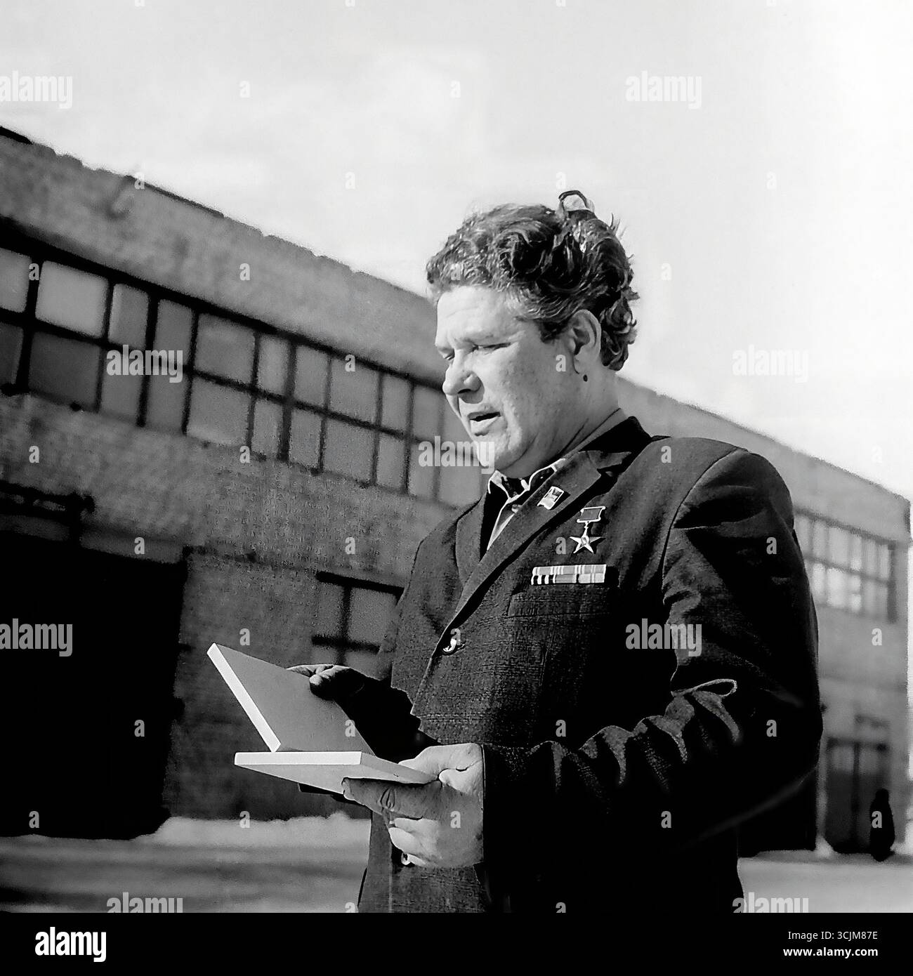 Ein Porträt eines Helden der Sozialistischen Arbeit vor seiner Hausfabrik in Slawjansk, 1976. Diese monumentale Aufnahme aus der Stagnation-Ära, die einen dekorierten Arbeitsveteranen mit Auszeichnungen auf der Brust einfängt, ist ein Symbol für die Verherrlichung der Arbeiterklasse, die höchsten Arbeitsleistungen und die kreative Kraft eines friedlichen Donbas Stockfoto