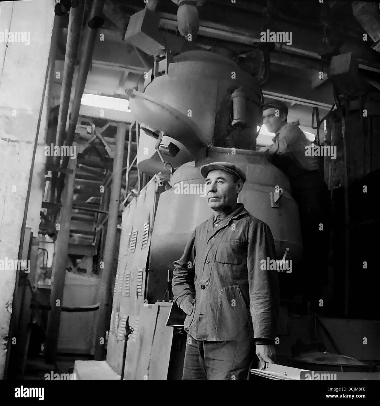 Ein monumentales Porträt eines erfahrenen Arbeiters vor dem Hintergrund einer Industrieeinheit in einer Fabrikwerkstatt in Slawjansk, 1976. Diese heroische Aufnahme aus der Stagnation-Ära ist ein Symbol für Handwerkskunst, Arbeitswürdigkeit und die kreative Macht der sowjetischen Schwerindustrie eines friedlichen Donbas Stockfoto