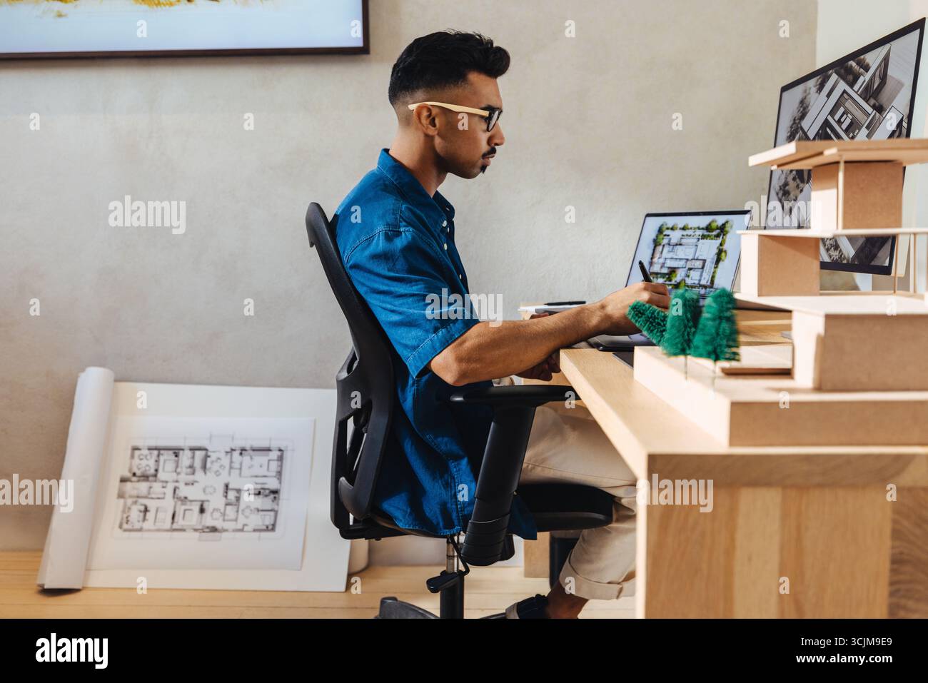 Ein junger Architekt, der fleißig in einem modernen Büro arbeitet und innovative Gebäudemodelle und -Layouts mit einem Computer und architektonischen Werkzeugen entwirft Stockfoto