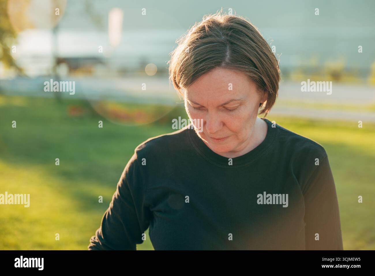 Frau mittleren Alters draußen im Sommersonnenlicht, mit schwarzem Hemd, nachdenklich und ruhig. Selektiver Fokus. Stockfoto
