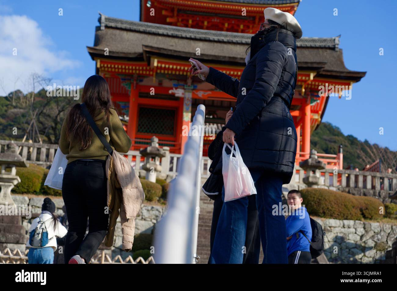 Besucher steigen in Richtung Kiyomizu-deras kupferfarbenes Tor auf, das von Steinlaternen eingerahmt wird Stockfoto